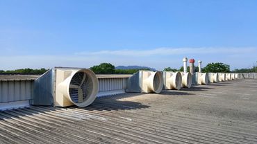Rooftop-mounted industrial exhaust fans in a row on a factory roof with hills in the background
