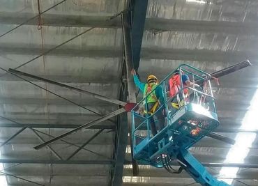 Industrial technician at height servicing rooftop ducting and cabling while wearing safety harness e