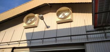 Worker installing a circular roof exhaust fan on a factory rooftop panel